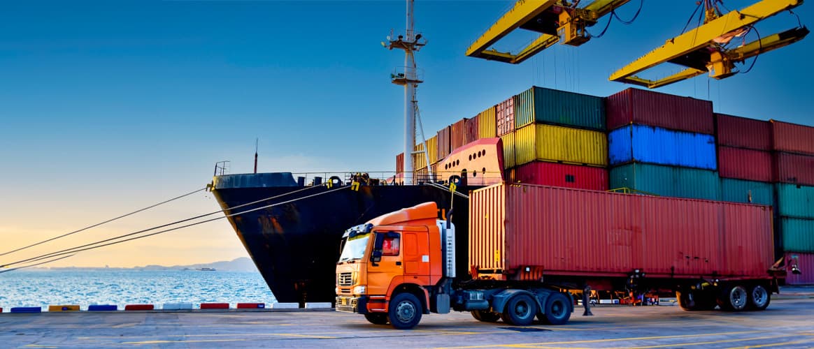 A containership unloads in a port as a articulated lorry truck carries off one of the cargo containers